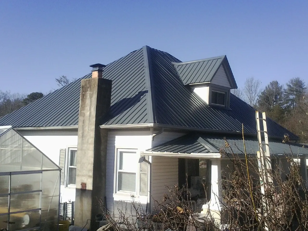 Dark blue standing seam metal roof on a white farmhouse with dormer — Slate & Tile Roof Repair by Roofing Brothers in Paullina
