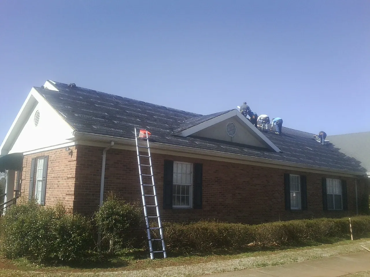 Crew tearing shingles off a brick ranch roof with a ladder set — Emergency Roof Repair work by our crew in Paullina