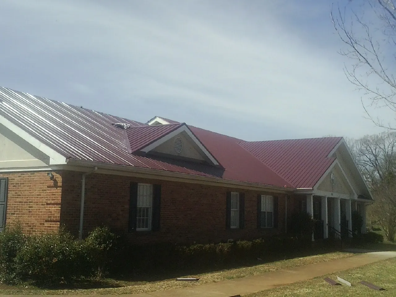Red metal roof with gabled entries on a long brick building, from a Hail Damage Roof Repair job in Paullina