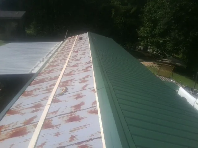 Old rusted panels beside newly installed green metal roofing — Wind Damage Roof Repair by Roofing Brothers in Paullina