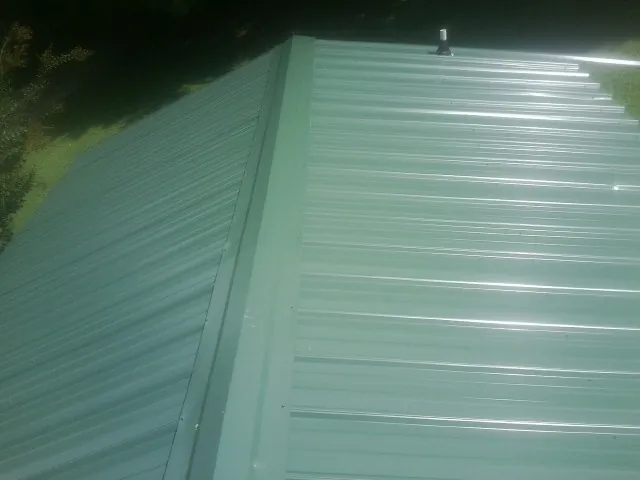 New green metal panels meeting at the ridge of a roof — Flat Roof Repair work by our crew in Paullina