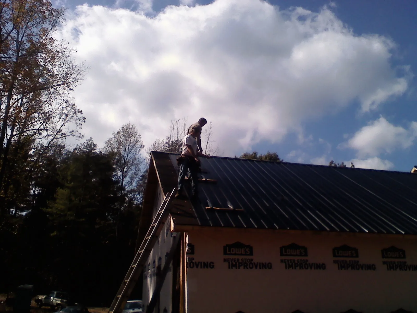 Roofer fastening dark metal panels high against a cloudy sky, from a Roof Inspection job in Paullina