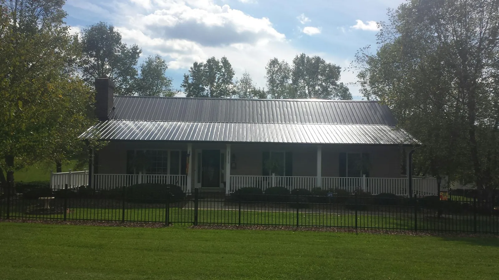 Gray metal roof on a brick ranch with a full width front porch — Gutter Guard Installation work by our crew in Paullina