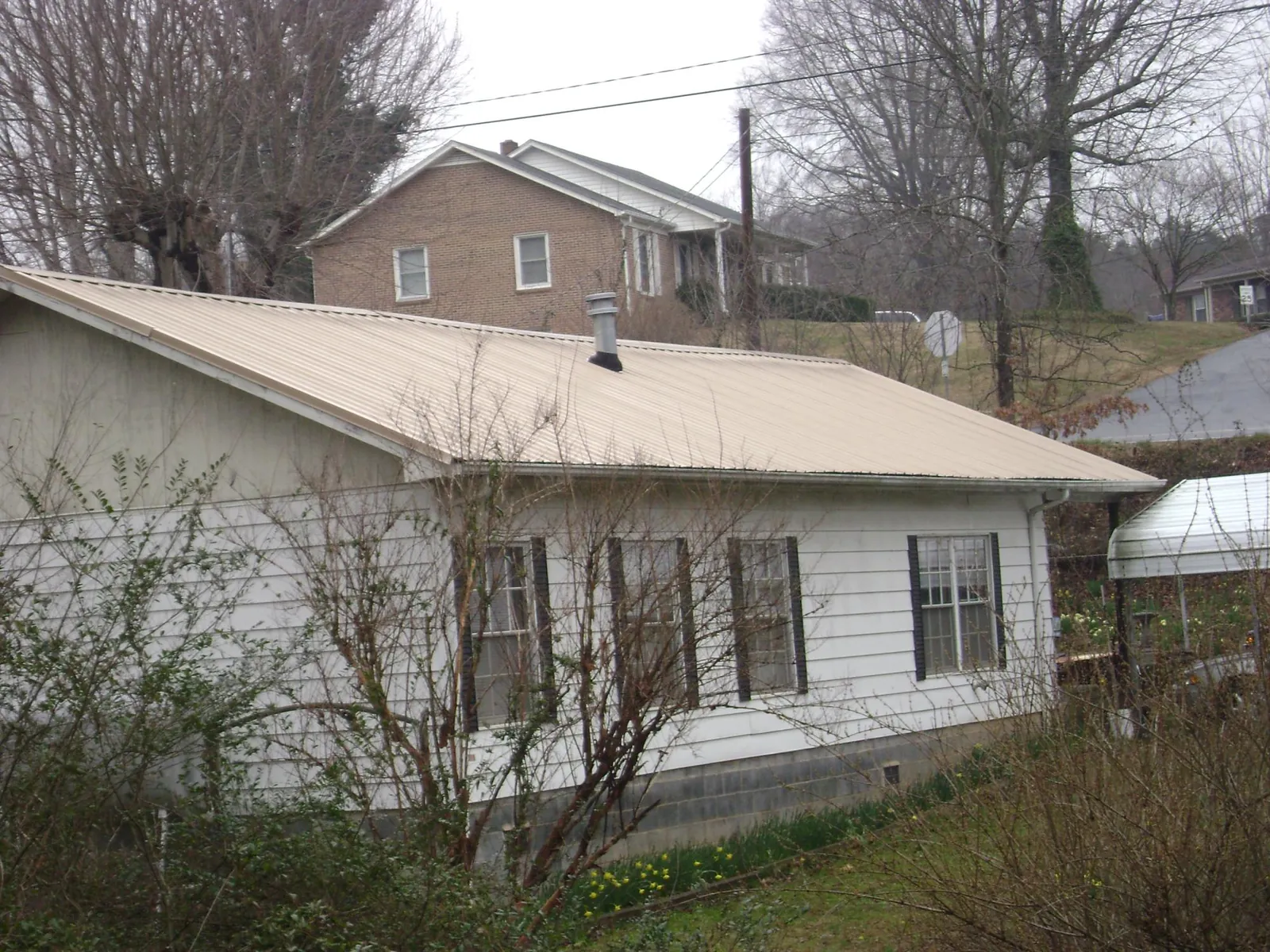 Tan metal roof on a white sided house set into a hillside — Commercial Roofing by Roofing Brothers in Paullina