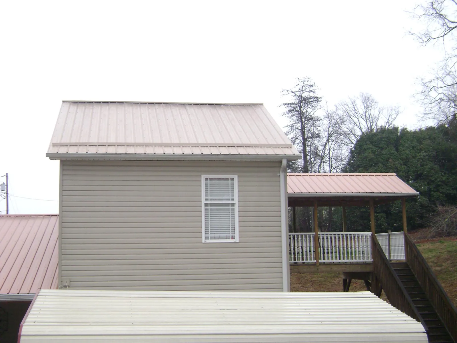Tan metal roofs on a two story addition and attached porch, from a Roof Replacement job in Paullina